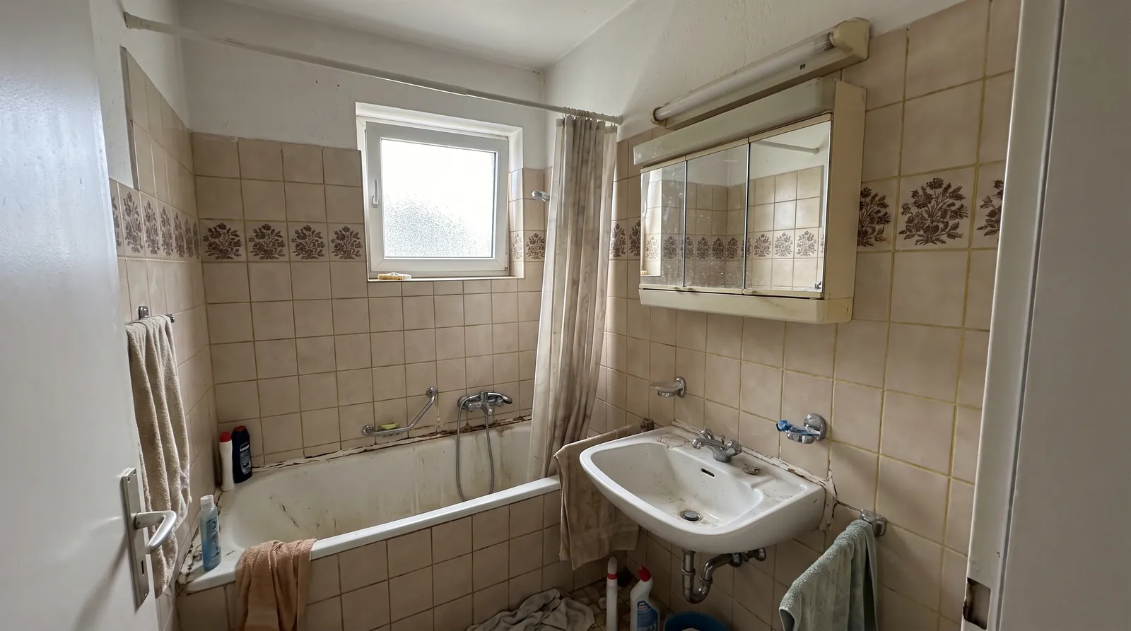 Badezimmer vor der Sanierung: vergilbte Fliesen, alte Badewanne mit Duschvorhang